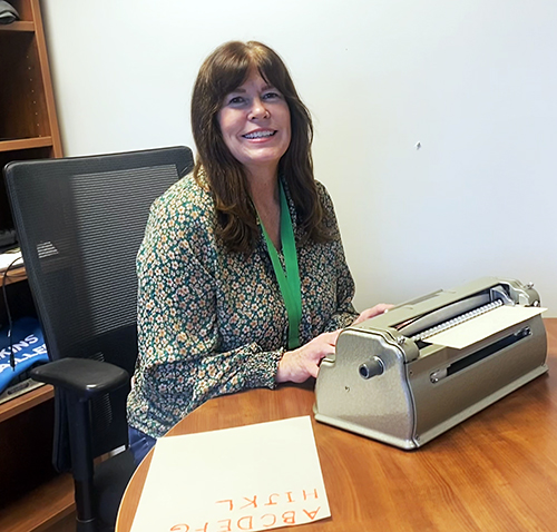 Instructor, Connie Michaels, pictured smiling behind a typewriter